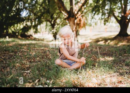 Wunderschönes kleines Kind, das am Sommertag mit Stöcken und Gras spielt Stockfoto