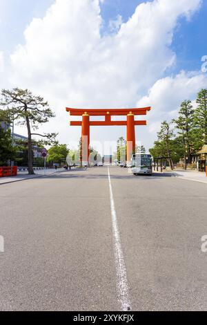 Ein großes oranges japanisches Torii-Tor auf der Jingu-Michi Straße umrahmt den historischen Heian-Schrein in der Ferne an einem sonnigen Tag in Kyoto, Japan. Vertikaler Cop Stockfoto