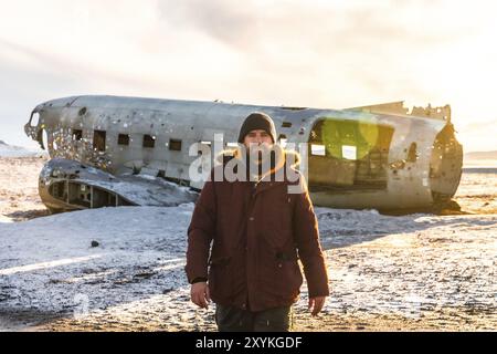 Ein Tourist, der im Winter in Island auf dem gefrorenen Solheimasandur-Strand auf dem abgestürzten Flugzeug spaziert Stockfoto