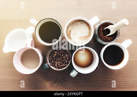 Mehrere Kaffeetassen und bunte Tassen mit Americano, Espresso, Latte und Cappuccino, Milchglas, geröstete Kaffeebohnen in Glasflasche, Holzlöffel Stockfoto