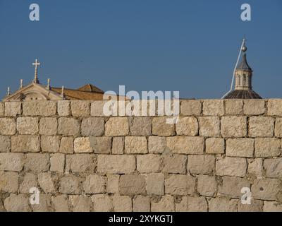 Massive Steinmauer vor historischen Gebäuden und Kirchturm unter einem klaren blauen Himmel, dubrovnik, Mittelmeer, Kroatien, Europa Stockfoto