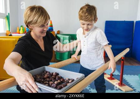 Junge mit Zerebralparese betreibt körperliche Rehabilitation und balanciert auf einem Balken, unterstützt von einem Therapeuten während einer Therapiesitzung Stockfoto