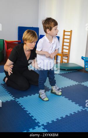 Junge mit Bewegungsstörungen nimmt an der Physiotherapie Teil und arbeitet mit Anleitung von Bobath Therapeut am Stehen und Gleichgewicht Stockfoto