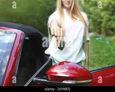 Glückliche junge, blonde Frau Betrieb Schlüssel zu ihrem Sportauto Stockfoto