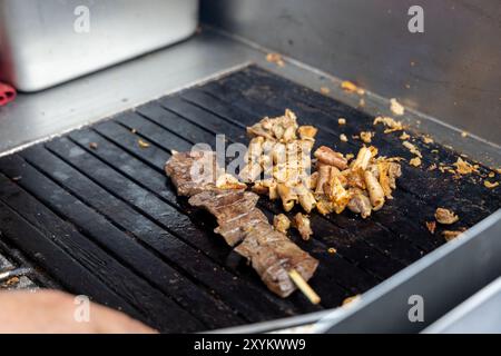 Eine Person kocht Antikuchos auf einem Grill. Das Fleisch wird auf Spießen gekocht und wird von anderem Fleisch umgeben Stockfoto