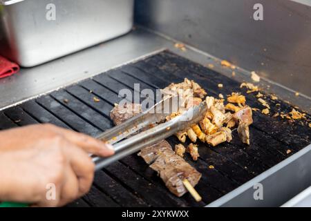 Eine Person kocht Antikuchos auf einem Grill. Das Fleisch wird auf Spießen gekocht und wird von anderem Fleisch umgeben Stockfoto