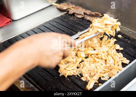 Eine Person kocht Antikuchos auf einem Grill. Das Fleisch wird auf Spießen gekocht und wird von anderem Fleisch umgeben Stockfoto