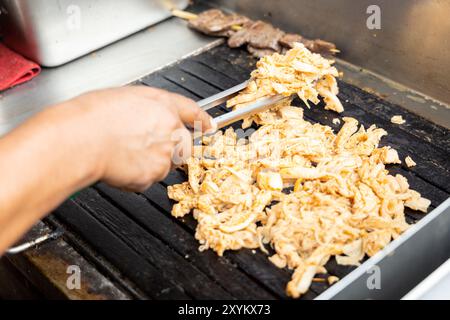 Eine Person kocht Antikuchos auf einem Grill. Das Fleisch wird auf Spießen gekocht und wird von anderem Fleisch umgeben Stockfoto