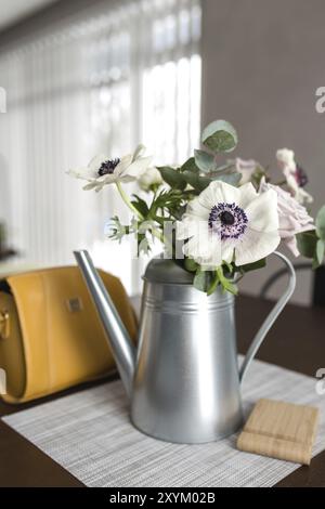 Zarte Anemonen Blumen in einer Metalltopf Vase auf dem Holztisch, gelbe Handtasche. Unscharfer Hintergrund Stockfoto