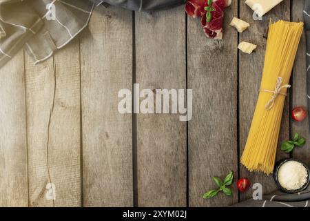 Italienische Küche Konzept flach Lay. Parmesan-Käsestückchen, geriebener Käse in schwarzer Schüssel, rohe Pasta, dünn geschnittener Schinken, Kirschtomatos, Basilikum lea Stockfoto