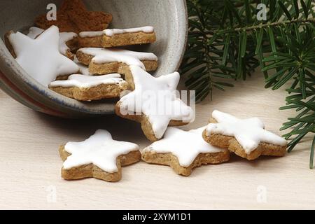 Zimtsterne, traditionelle weihnachtsplätzchen, auf deutsch zimtsterne genannt, fallen aus einer Steingut-Schüssel auf einem Holzbrett, Kiefernzweige in der Ba Stockfoto