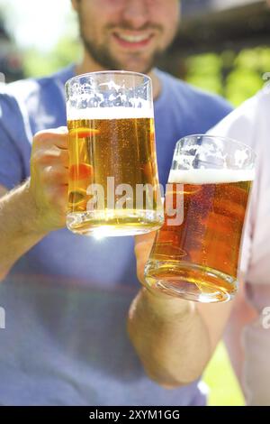 Nahaufnahme von zwei jungen Männern in Freizeitkleidung, die eine Brille mit Bier ausstrecken und im Freien lächeln Stockfoto