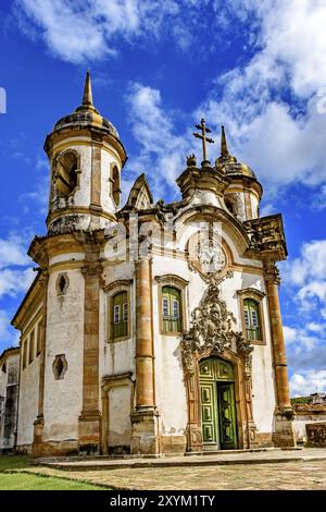Fassade der Kirche von Sao Francisco de Paula in Ouro Preto, Minas Gerais mit seinen Fenstern, großen Holztüren, Steinbogen, Türmen und barocken Skulpturen Stockfoto