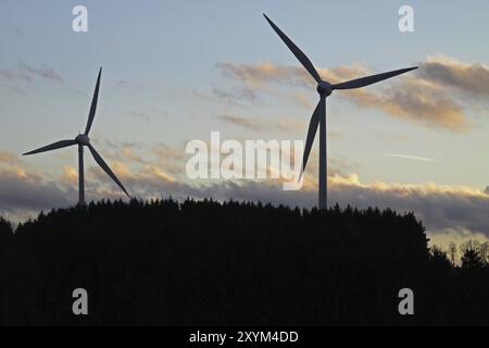 Silhouetten von zwei Windturbinen hinter einem Wald Stockfoto