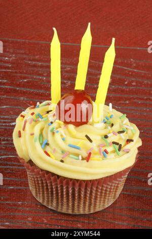 Geburtstagskuchen mit Zitronenbuttercreme, Streuseln, kandierten Kirschen und drei Kerzen. Auf rotem Hintergrund. Selektiver Fokus Stockfoto