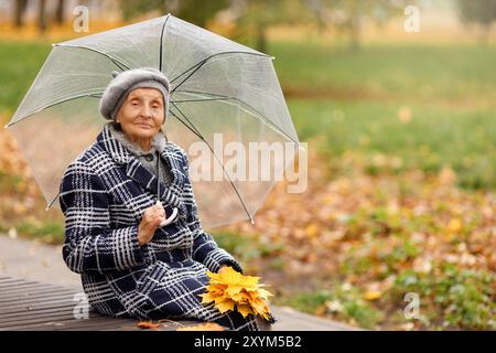 Ältere Frau im grauen Mantel mit Regenschirm im Herbst Stockfoto