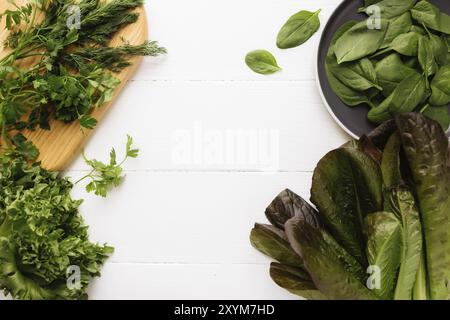 Flach legen mit Schneidebrett und Schüssel mit frischen grünen Salatblättern Spinat und Salat, Romaine und Petersilie, Basilikum auf weißem Hintergrund. Gesundes Gemüse Stockfoto