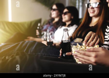 Eine Gruppe von Freunden in 3D-Brillen schaut sich einen Film an, lächelt, lacht. Essen und Trinken, während Sie sich einen Film im Kino ansehen. Mädchen essen Popc Stockfoto