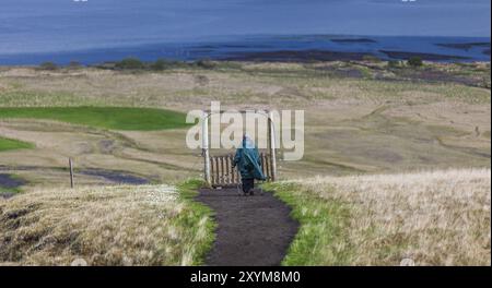 AUSTURLAND, ISLAND, 20. JUNI: Eine ältere Frau in einem grünen cape und mit Wanderstöcken wandert am 20. Juni 2013 in Austurla in der Nähe des Wasserfalls Hengifoss Stockfoto