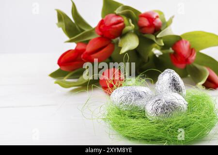 Rote Tulpen und Eier in einem Nest auf weißem Holzbrett, osterhintergrund Stockfoto