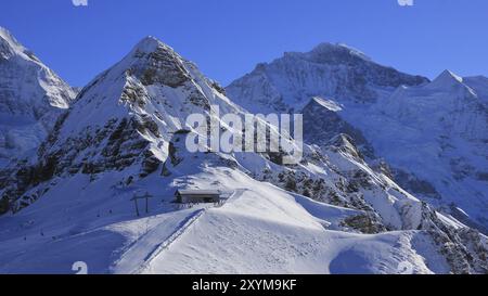 Winterszene in Grindelwald, Schweizer Alpen. Schneebedeckte Berge Lauberhorn und Jungfrau, Gipfelstation einer Seilbahn Stockfoto