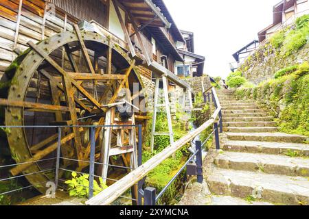 Ein traditionelles, sich drehendes hölzernes Wasserrad, das von einem Bach neben einem Steinweg auf der alten Nakasendo-Straße in der Poststadt Magome verschwimmt wird. Stockfoto