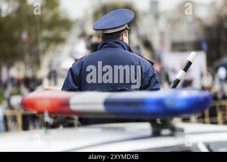 Polizist des Sicherheitsdienstes mit Verkehrsstab, der die Straße in der Nähe des Polizeiwagens mit Sirenenlicht bewacht Stockfoto