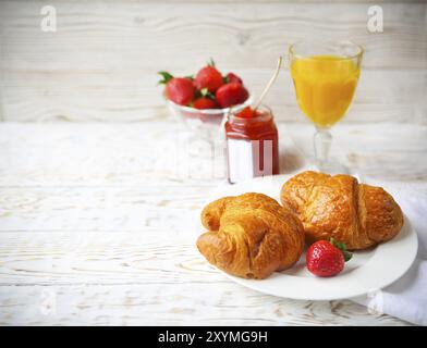 Zwei leckere Croissants auf dem Teller und Erdbeermarmelade auf hölzernem Hintergrund Stockfoto