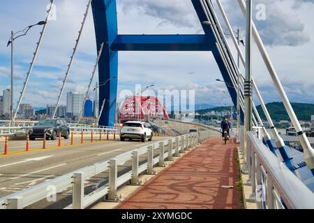 Sokcho, Südkorea - 28. Juli 2024: Ein Radfahrer und Fahrzeuge überqueren die Seorak Grand Bridge und fahren in Richtung der roten Bögen der Geumgang Grand Bridge. Stockfoto