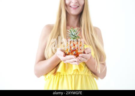Portrait einer hübschen jungen Frau im gelben Kleid und Strohhut Holding frische Ananas Stockfoto