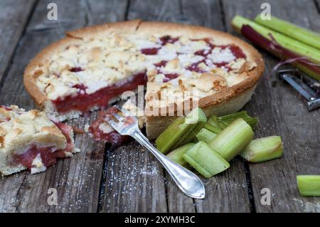 Geschnittener Rhabarberkuchen auf einem Holzbrett. Daneben sind geschälte Rhabarber-Stiele und -Stücke. Geschnittener Rhabarberkuchen auf einem Holzbrett. Zusätzlich werden frisch geschälte r Stockfoto