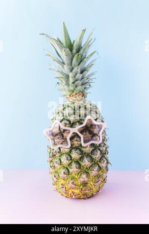 Reise- und Urlaubskonzept mit Ananas in Sonnenbrillen. Rosa Gläser in Form eines Sterns. Entspannung am Meer. Rosa und blauer Hintergrund Stockfoto