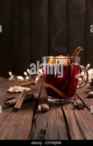 Weihnachtszeit Konzeptfoto. Glasbecher oder Becher mit Glühwein innen auf Holztisch und Hintergrund. Girlanden, Dekorationen, Zimt, Haselnuss, Die Stockfoto