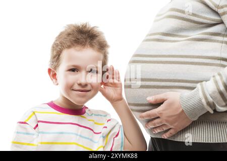 Schwangerschaft und neues Lebenskonzept, kleiner neugieriger lächelnder Kinderjunge, der seinem schwangeren Mutterleib zuhört Stockfoto