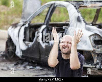 Weinender, verärgerter kaukasier bei einem Verkehrsunfall oder Brandstiftung Feuer verbrannten Rad Auto Auto-Trödel Stockfoto