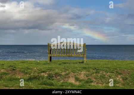 Eine Bank mit einem Regenbogen über der Nordsee Küste, im Benthall, Northumberland, England, UK gesehen Stockfoto