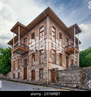 Ein elegantes historisches Gebäude in Shaki, Aserbaidschan, mit traditioneller Architektur mit detaillierten Holzbalkonen und großen Fenstern vor dem Hintergrund eines bewölkten Himmels. Stockfoto