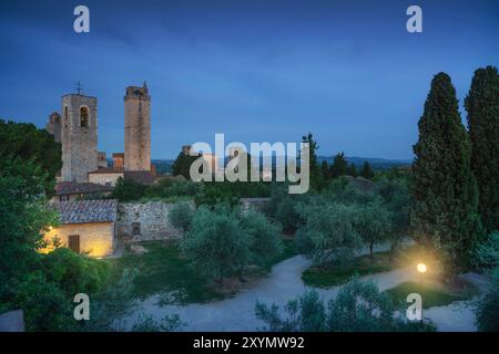 Nächtlicher Blick auf San Gimignano mit seinen Türmen aus einem öffentlichen Park mit Olivenbäumen. Provinz Siena, Toskana, Italien Stockfoto