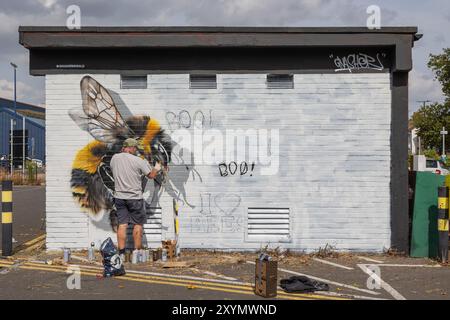 Southend on Sea, Großbritannien. 30. August 2024. Ein Straßenkünstler malt ein realistisches Bienengemälde auf eine weiße Ziegelwand. Sprühdosen, die um ihn herum verstreut sind, deuten auf aktive Arbeit hin. Der Körper der Biene ist detailliert, die Flügel sind noch in Bearbeitung. City Jam wird offiziell eröffnet und über 200 Künstler aus aller Welt malen Wandbilder. Penelope Barritt/Alamy Live News Stockfoto