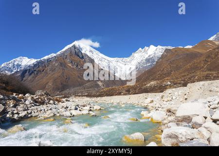 Ansicht des Langtang Lirung Peak, Teil des schneebedeckten Himalaya Gebirges hinter schnell fließenden Fluss der Gletscherwasser in großer Höhe in Nepal-Landschaft. Stockfoto