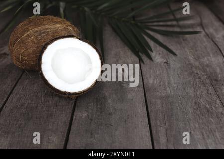 Gebrochene Kokosnüsse auf grauem hölzernem Hintergrund mit Palmblatt. Weißes Kokosnussfleisch. Stockfoto