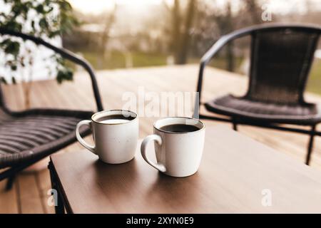 Zwei Tassen Kaffee auf dem Tisch auf der braunen Holzterrasse während des Abenduntergangs. Entspannungskonzept, Café oder Restaurant Stockfoto