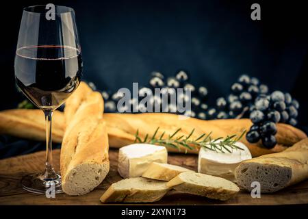 Ein Glas Rotwein mit Trauben, Baguette und Käse Stockfoto