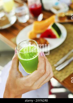 Frau mit Glas ein grüner Saft in der Hand Hand beim Hving Frühstück am Morgen Stockfoto