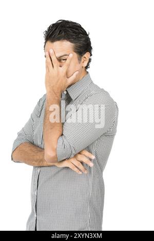 Profil eines gut aussehenden latino-Mannes in legeren Kleidern, Button-Down-Hemd, Hand bedeckendes Gesicht, Auge blickend durch gespaltenen Finger und zeigt schüchtern, feurig Stockfoto