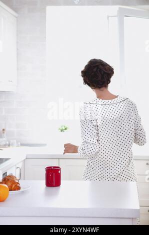 Blick auf gesichtslose Brunette in legerer Kleidung Fenster öffnen genießen frischen Morgen beim stehen in einer komfortablen Küche mit weißen Möbeln und Stockfoto