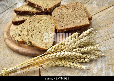 Blick von oben auf geschnittenes Vollkornbrot auf einem Holztisch. Verschiedene Brotsorten und Getreideohren Stockfoto