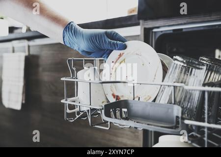 Nahaufnahme des Einfüllens, Einführens, Einfüllens von schmutzigem Geschirr, Einsetzens weißer Teller in den geöffneten, in Edelstahl integrierten Geschirrspüler-mac Stockfoto