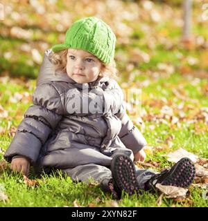 Kind, das im Herbstpark auf Gras sitzt Stockfoto