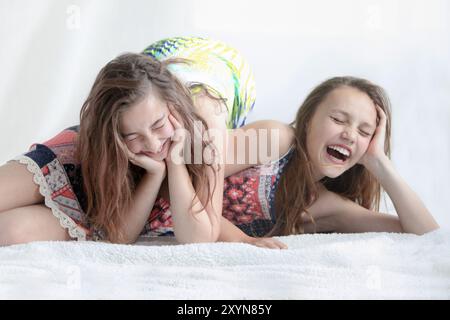 Porträt von zwei glücklichen kleinen Mädchen, die in einer weißen Decke liegen, lachen und auf dem hellen Hintergrund herumlächeln Stockfoto